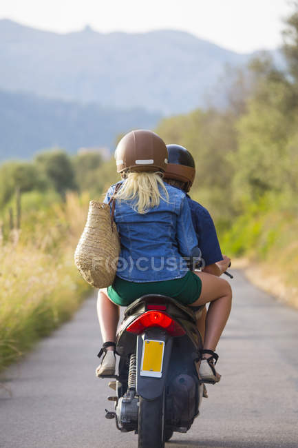 Vista trasera de pareja joven montando ciclomotor en carretera rural - foto de stock