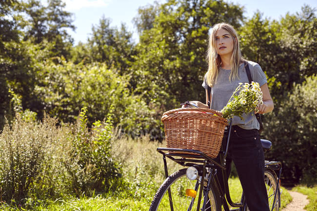 Porträt einer jungen Frau auf dem Fahrrad, die von einem Feldweg auf dem Land blickt — Stockfoto