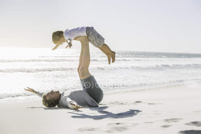 Father lying on beach lifting son — Stock Photo
