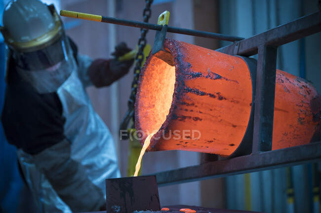Male foundry worker pouring bronze melting pot in bronze foundry — Stock Photo