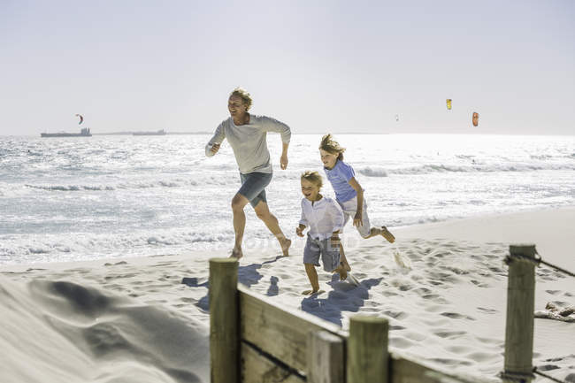 Padre e hijos corriendo en la playa - foto de stock