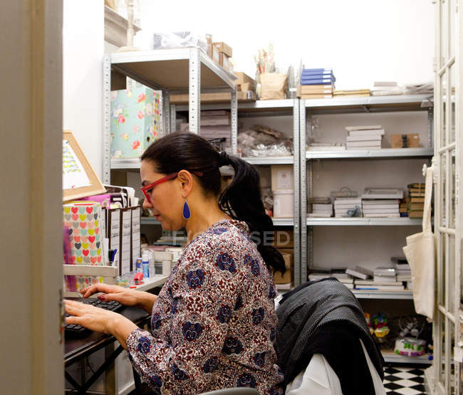 Donna piccolo imprenditore digitando sulla tastiera del computer in magazzino negozio di souvenir — Foto stock