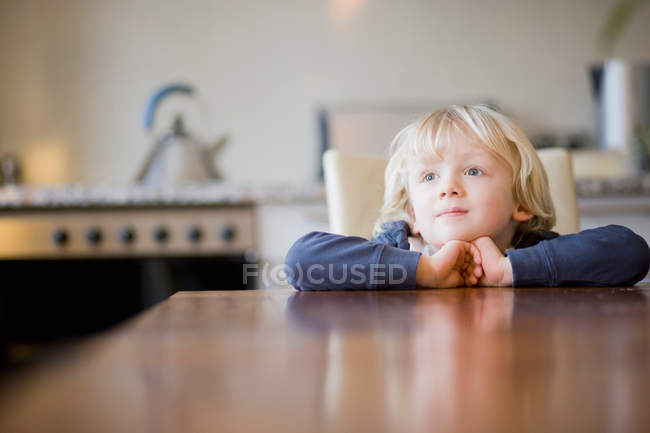 Menino olhando sobre a borda da mesa em casa — Fotografia de Stock