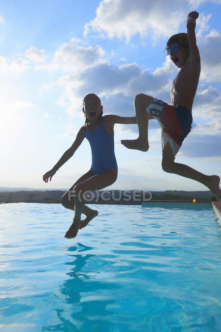 Девочка и брат прыгают в бассейн, Буонконвенто, Тоскана, Италия — стоковое фото