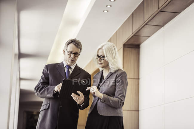 Femme d'affaires et homme utilisant une tablette numérique dans un couloir de bureau — Photo de stock