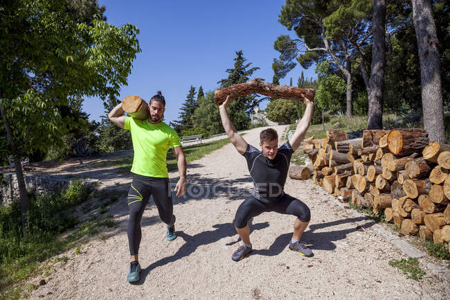 Due giovani uomini che fanno allenamento di sollevamento pesi con tronchi nella foresta, Split, Dalmazia, Croazia — Foto stock