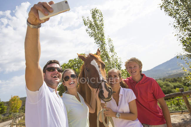 Groom et ses amis prenant smartphone selfie avec cheval dans les écuries rurales — Photo de stock