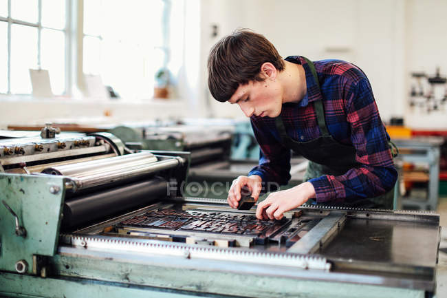 Jovem trabalhando na máquina de tipografia em oficina de artes do livro — Fotografia de Stock