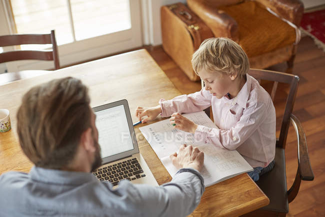 Батько допомагає синові з домашнім завданням в домашньому офісі — стокове фото