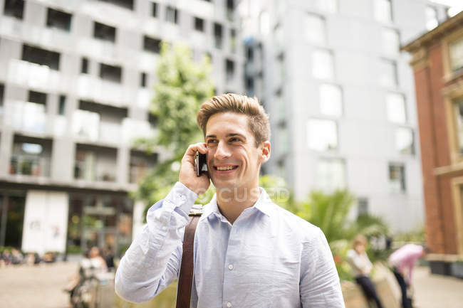 Young businessman talking on smartphone outside city office, London, UK — Stock Photo