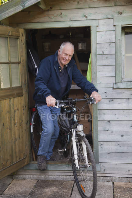 Senior man on bike by shed — Stock Photo
