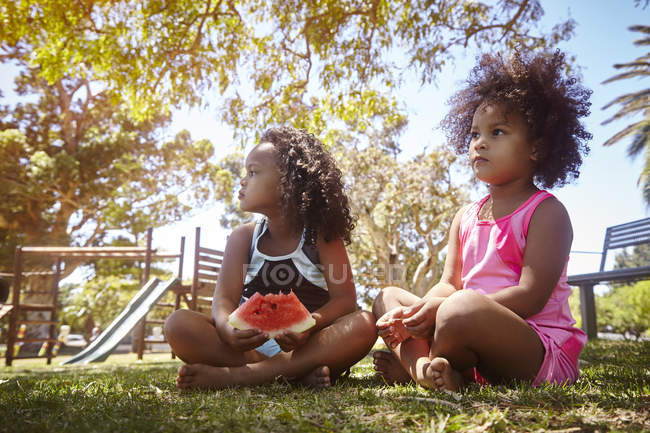 Две молодые сестры, сидя на траве, едят арбуз — стоковое фото