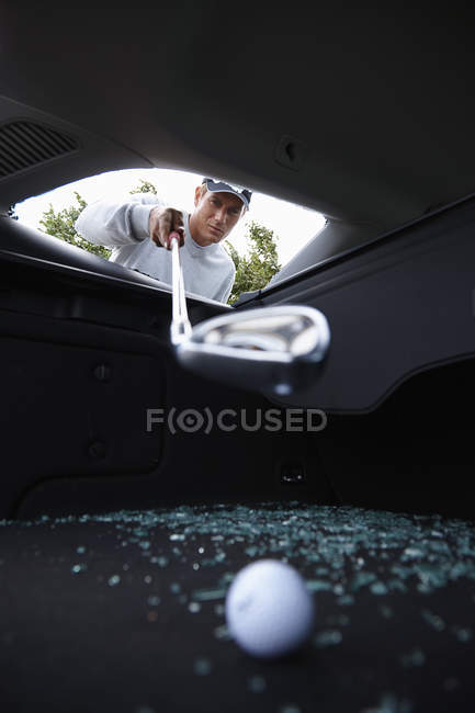 Golfer using golf club to retrieve golf ball through smashed car window — Stock Photo