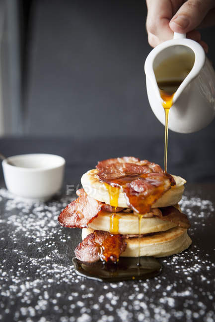 Female hand pouring maple syrup over breakfast bacon crumpet on slate — Stock Photo