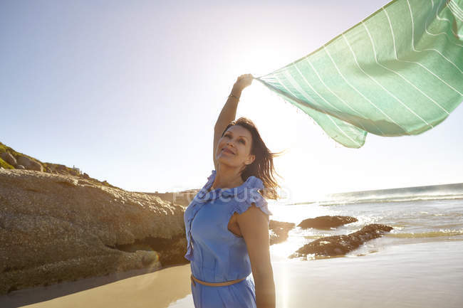 Зрелая женщина, стоящая на пляже, держа чистый шарф в воздухе, Кейптаун, Южная Африка — стоковое фото