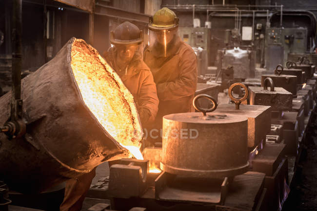 Two workers pouring molten metal from flask in foundry — Stock Photo