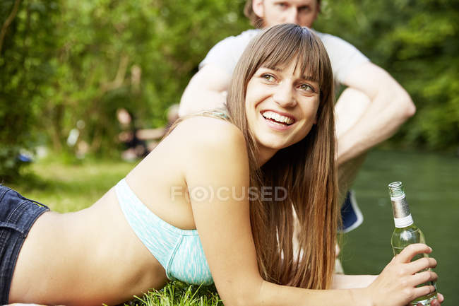 Пара розслабляється в парку, молода жінка тримає скляну пляшку — стокове фото