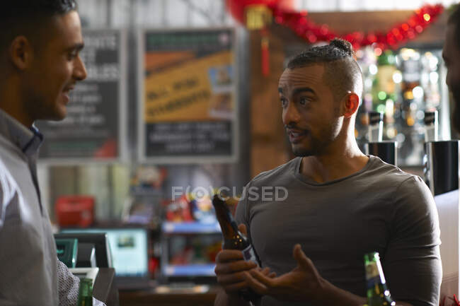 Joven en casa pública sosteniendo botella de cerveza hablando con un amigo - foto de stock
