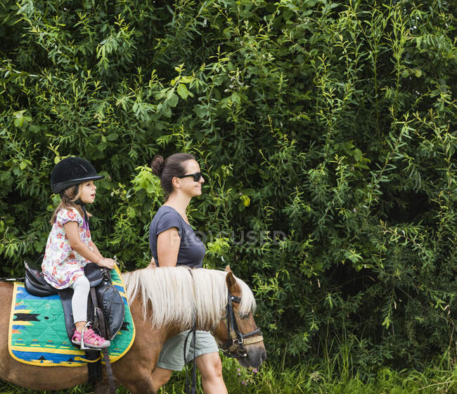 Side view of mother guiding daughter riding horse — Stock Photo