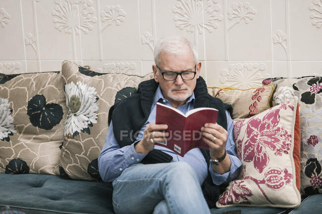 Senior man reading book on couch — Stock Photo