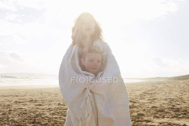 Portrait of two sisters wrapped in blanket on beach, Camber Sands, Kent, UK — Stock Photo