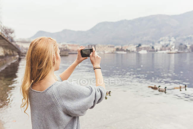 Mujer joven fotografiando desde la orilla del lago, Lago Como, Italia - foto de stock