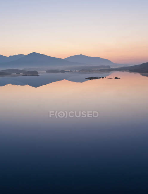 Montanhas refletidas em lago imóvel durante o pôr do sol — Fotografia de Stock