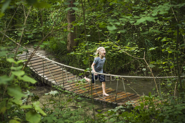 Menino correndo através de ponte de corda de pedestre na floresta — Fotografia de Stock
