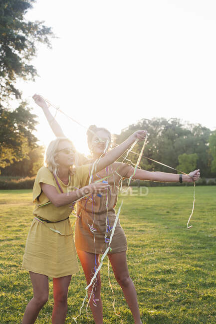 Due giovani amiche che si avvolgono in stelle filanti alla festa nel parco — Foto stock