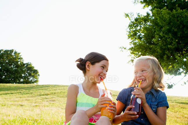 Смеющиеся девушки пьют сок на открытом воздухе — стоковое фото
