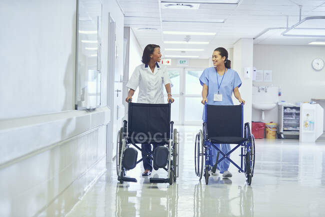 Female orderlies pushing wheelchairs along hospital corridor — Stock Photo