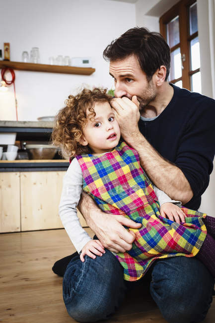 Mature man whispering to his daughter in kitchen — Stock Photo
