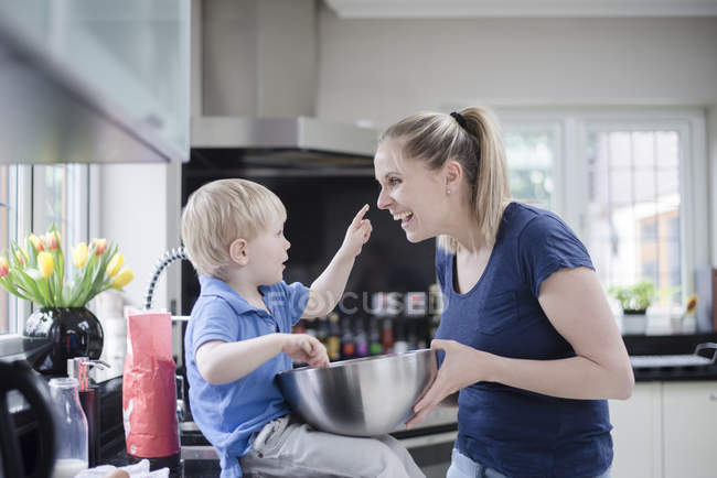 Mother and son fooling around whilst baking, son putting mixture on mother's nose — Stock Photo