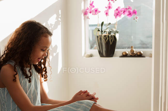Menina no quarto na parede perto da janela com flores de orquídea — Fotografia de Stock