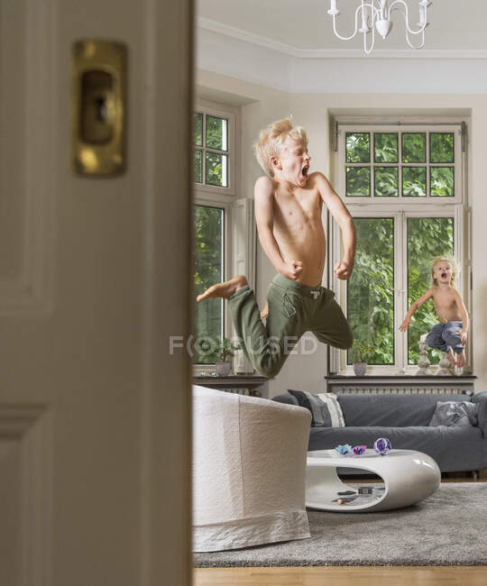 Chicos en la sala de estar saltando en el aire - foto de stock