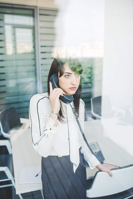 Office window view of young businesswoman talking on landline — Stock Photo