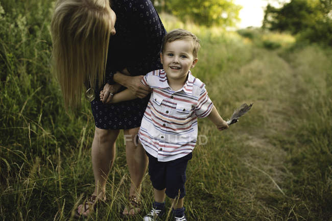 Madre inclinándose a su hijo con un puñado de plumas en el prado - foto de stock