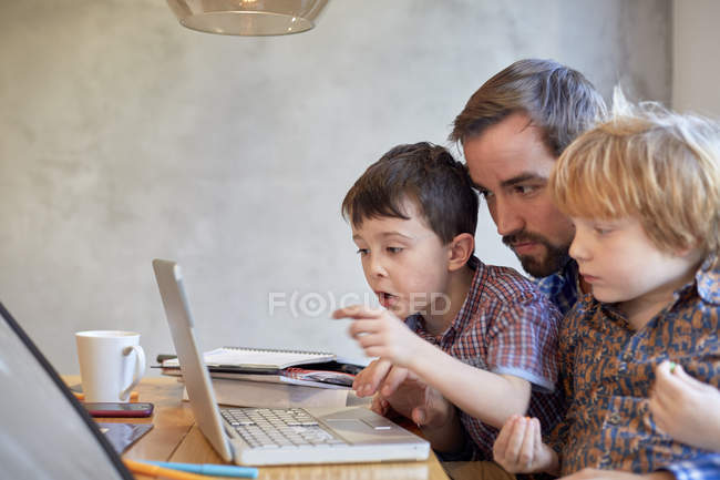 Homem adulto médio olhando para laptop com dois filhos na mesa de jantar — Fotografia de Stock