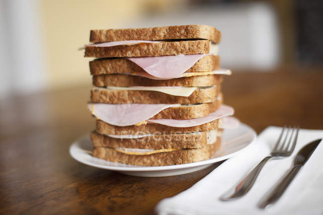 Стопка бутербродов с ветчиной на тарелке с столовыми приборами — стоковое фото