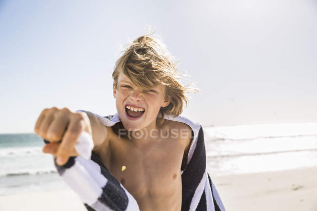 Niño en la playa envuelto en toalla boca abierta mirando a la cámara - foto de stock
