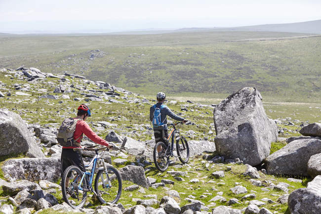 Rear view of cyclists walking bicycles down rocky hillside — Stock Photo