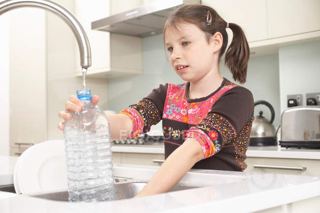 Дівчина заповнює пляшку води на кухні — стокове фото