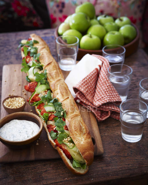 Tandoori chicken baguette and glasses of water on wooden table — Stock Photo