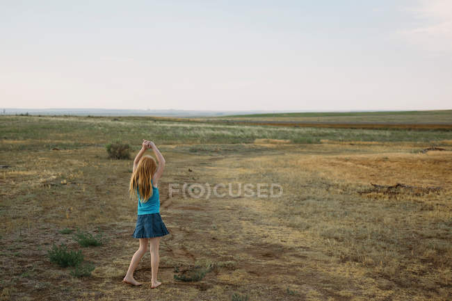 Rear view of girl on rural landscape playing alone — Stock Photo