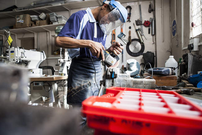Молодий чоловік використовує кутову шліфувальну машину в майстерні по ремонту — стокове фото