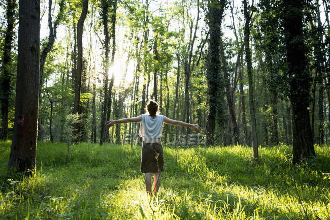 Vue arrière d'une jeune femme avec les bras ouverts dans la forêt, Vogogna, Verbania, Piemonte, Italie — Photo de stock