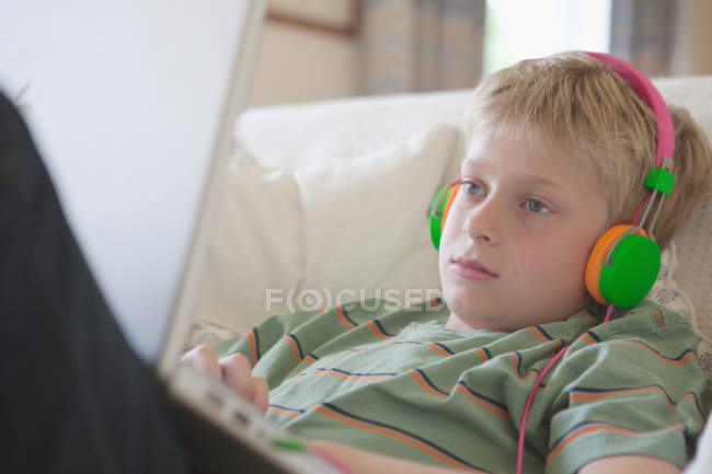 Niño escuchando los auriculares en el ordenador portátil - foto de stock