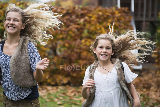 Dos hermanas con el pelo largo y rubio corriendo en el jardín de otoño - foto de stock