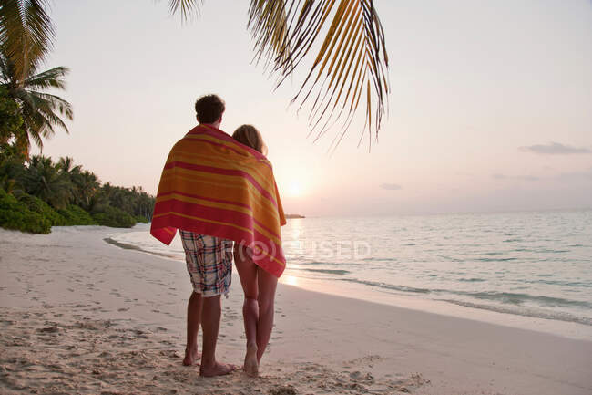 Pareja compartiendo toalla en la playa tropical - foto de stock