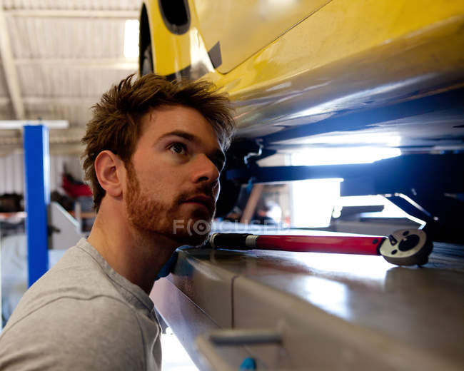 Masculino mecânico olhando embaixo do carro esporte — Fotografia de Stock